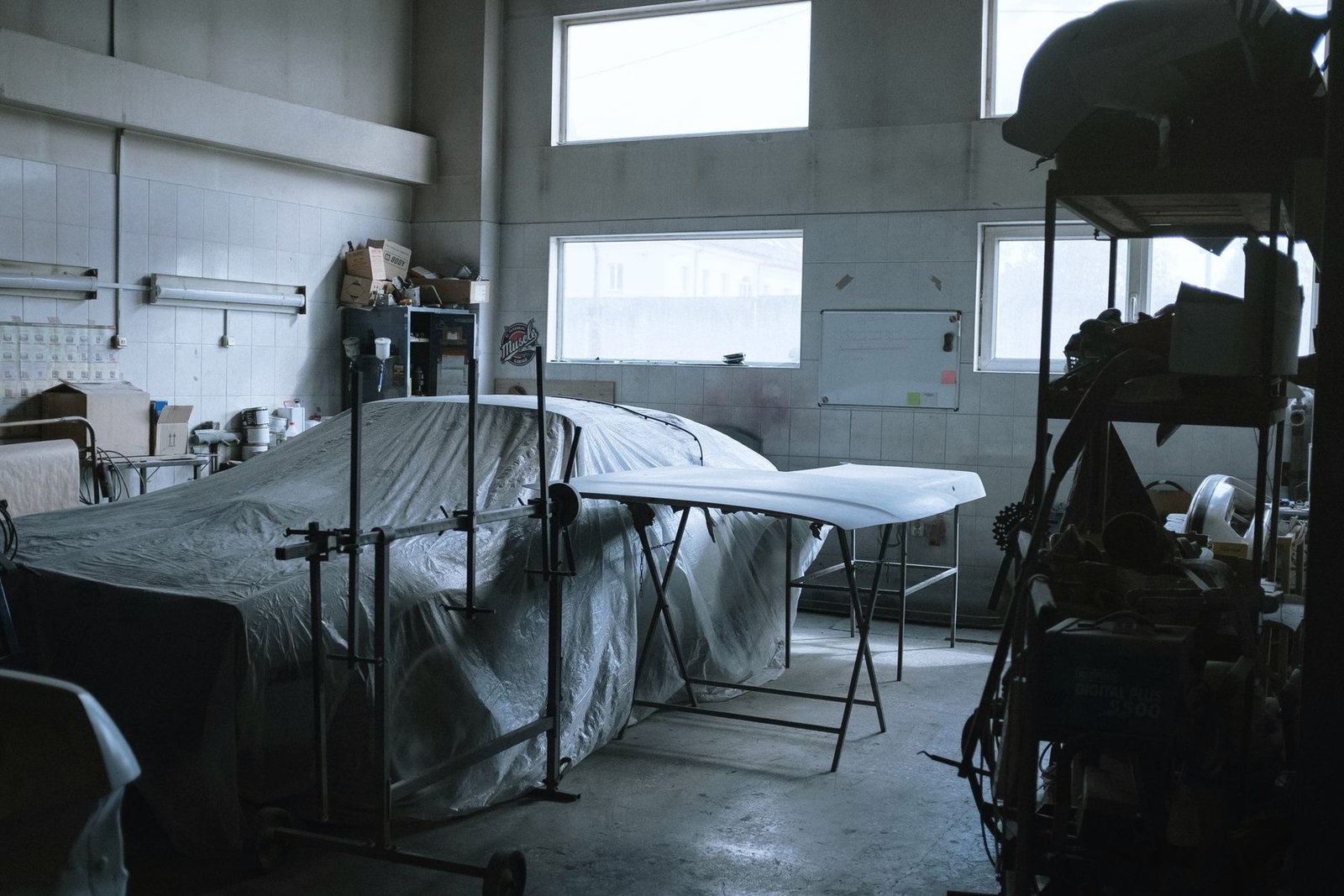 A car under a cover in a quiet repair shop with tools and stands