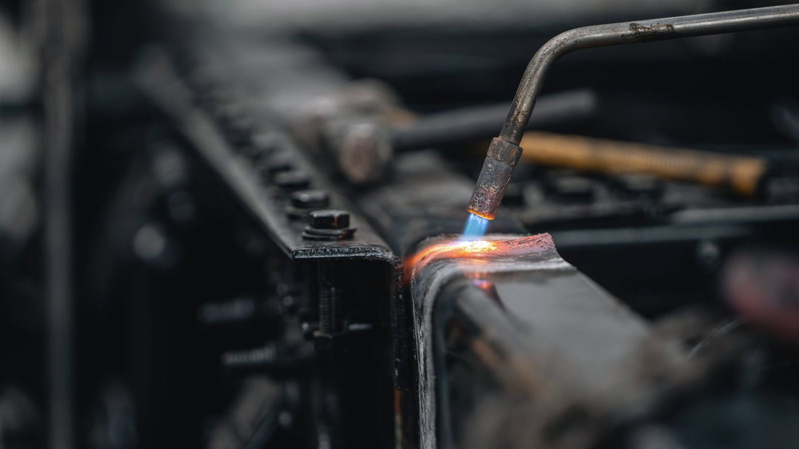 A welding torch with a blue flame working on a steel part