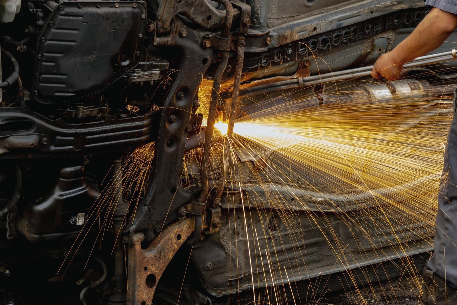 Sparks from welding under a lifted car, worker crouched beside it